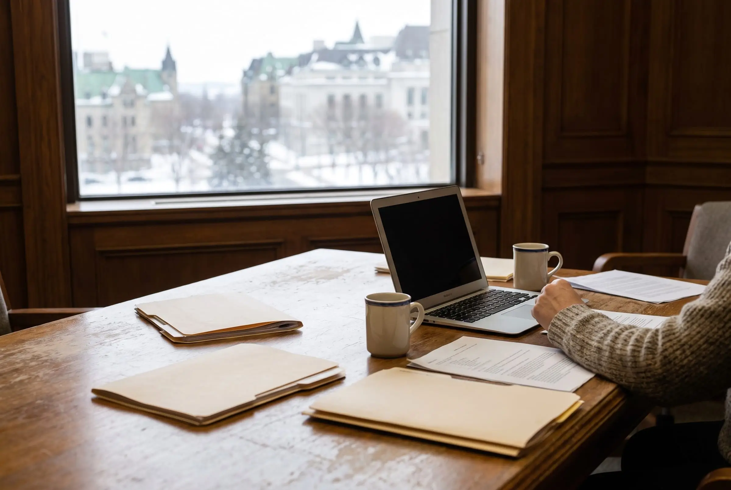 Folders and a laptop on a meeting table by a window