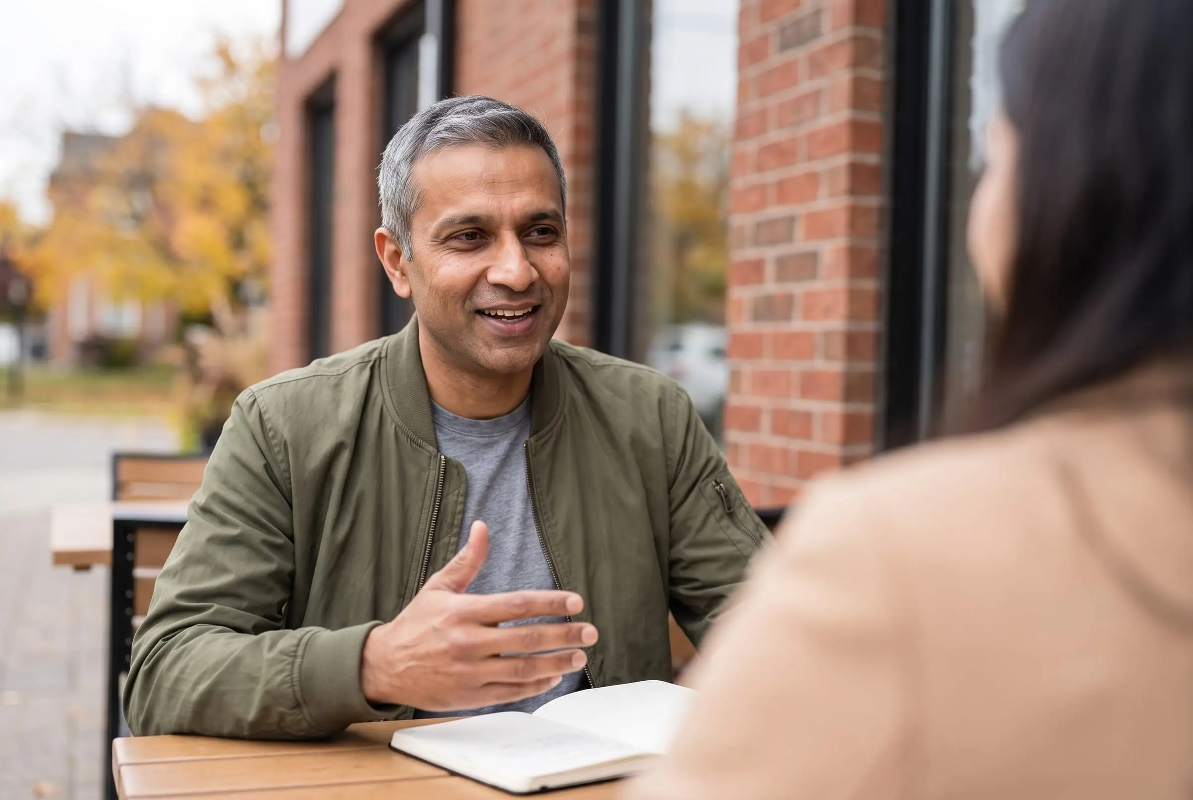 Arjun Mehta explaining a plan with a notebook at a café table
